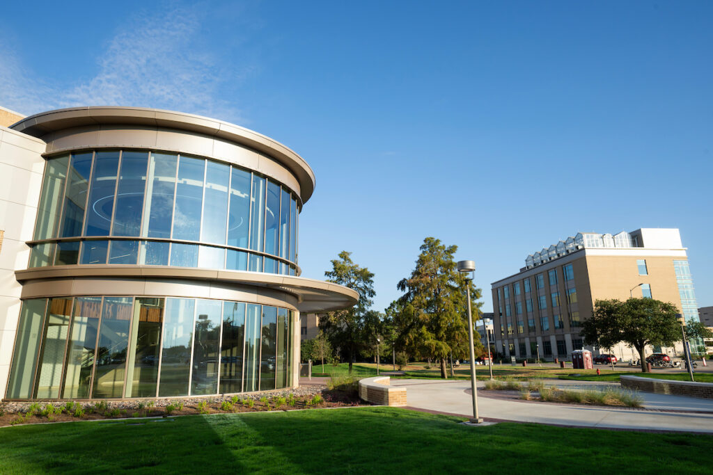 The glass-paneled circular atrium of the Norman E. Borlaug building stands against a bright blue sky