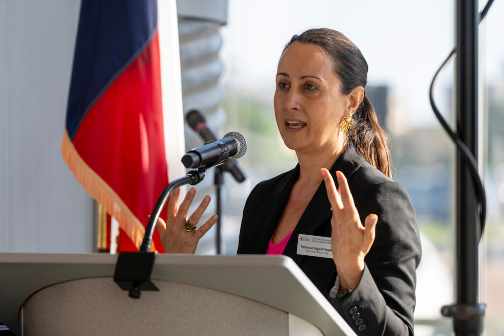 Rebecca Seguin-Fowler stands speaking behind a podium, gesturing with her hand
