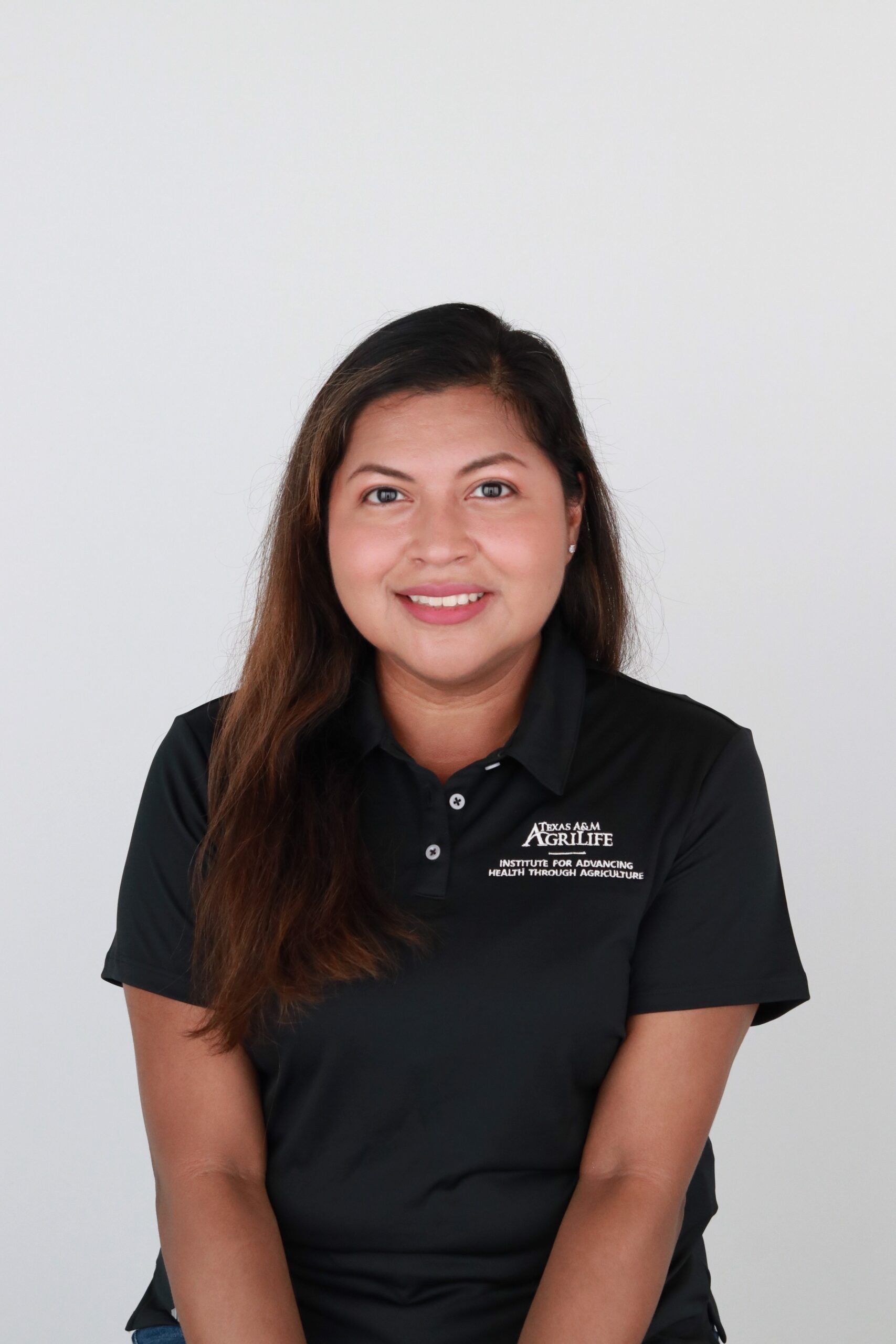 A woman with dark hair wears a black polo embroidered with the IHA's logo and smiles at the camera in front of a white background