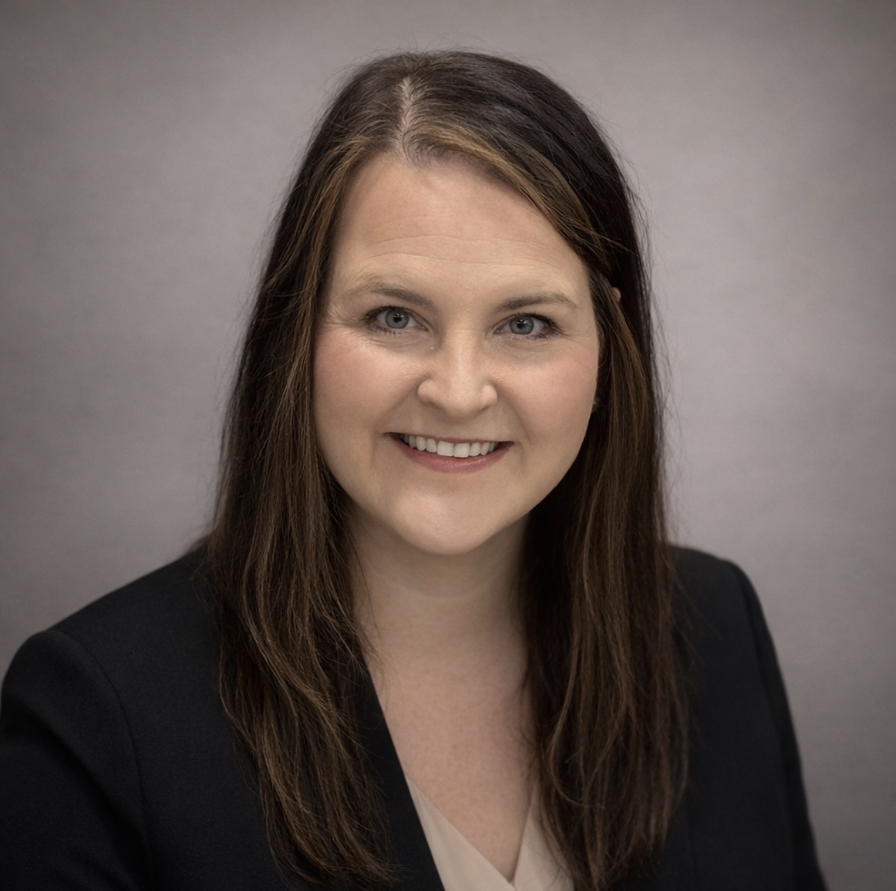 Woman with brown hair wears black blazer and smiles at camera